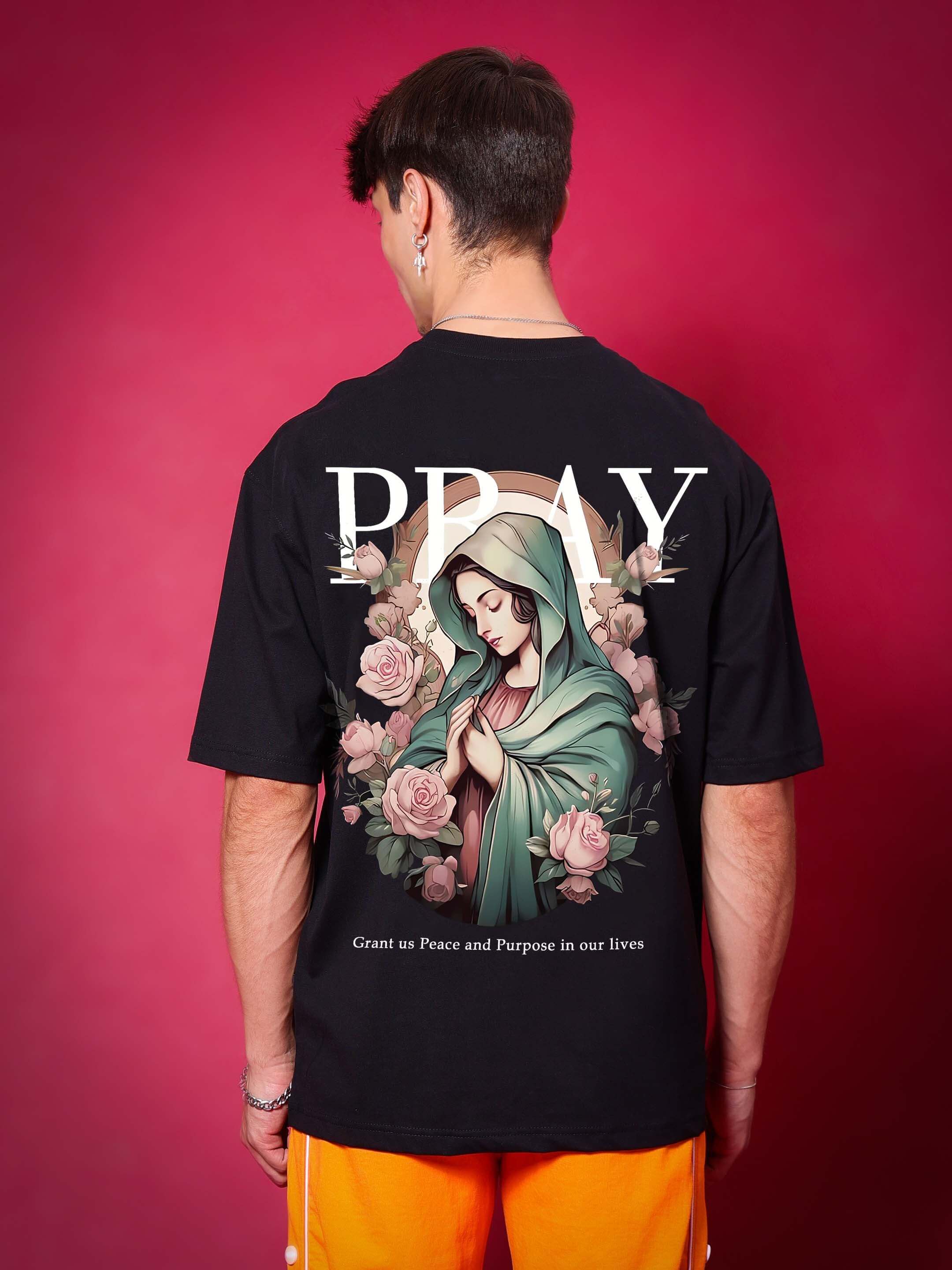 Black over-sized T-shirt with "Pray" and a serene image on back, made from premium heavy gauge fabric. Model wearing orange pants.