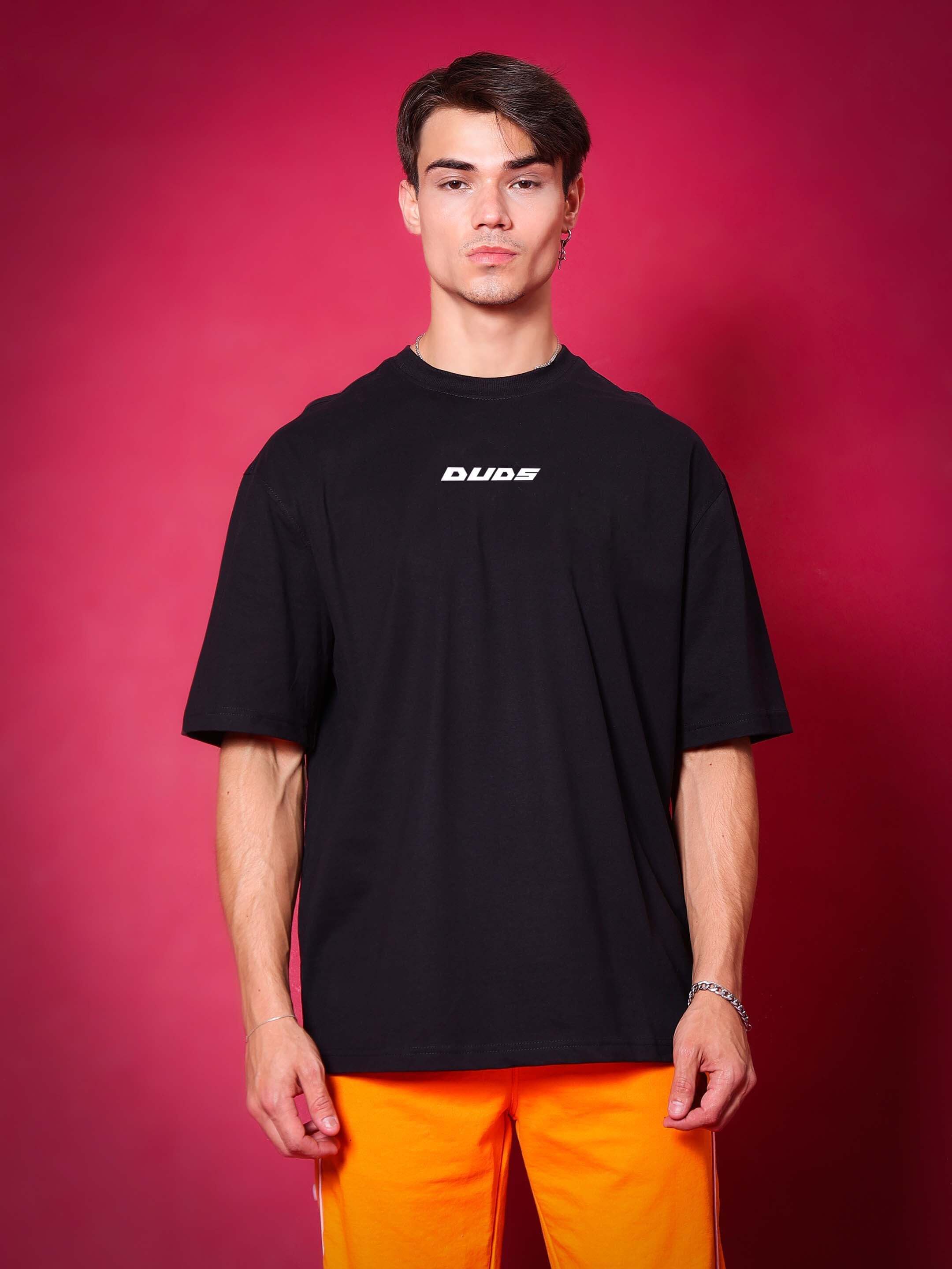Black oversized T-shirt in premium cotton, modeled against a vibrant red background, paired with bright orange pants.
