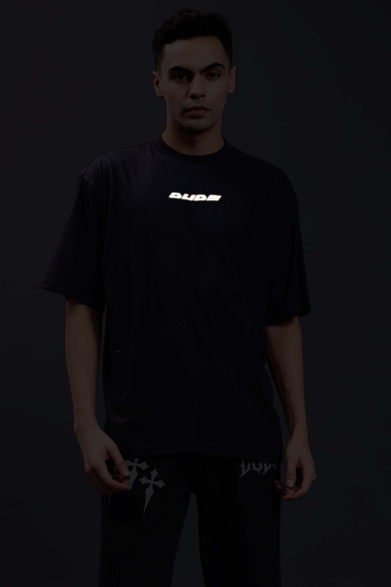 Model wearing PULSATING RHYTHMS REFLECTOR OVER-SIZED T-SHIRT BLACK with glowing reflector detail.