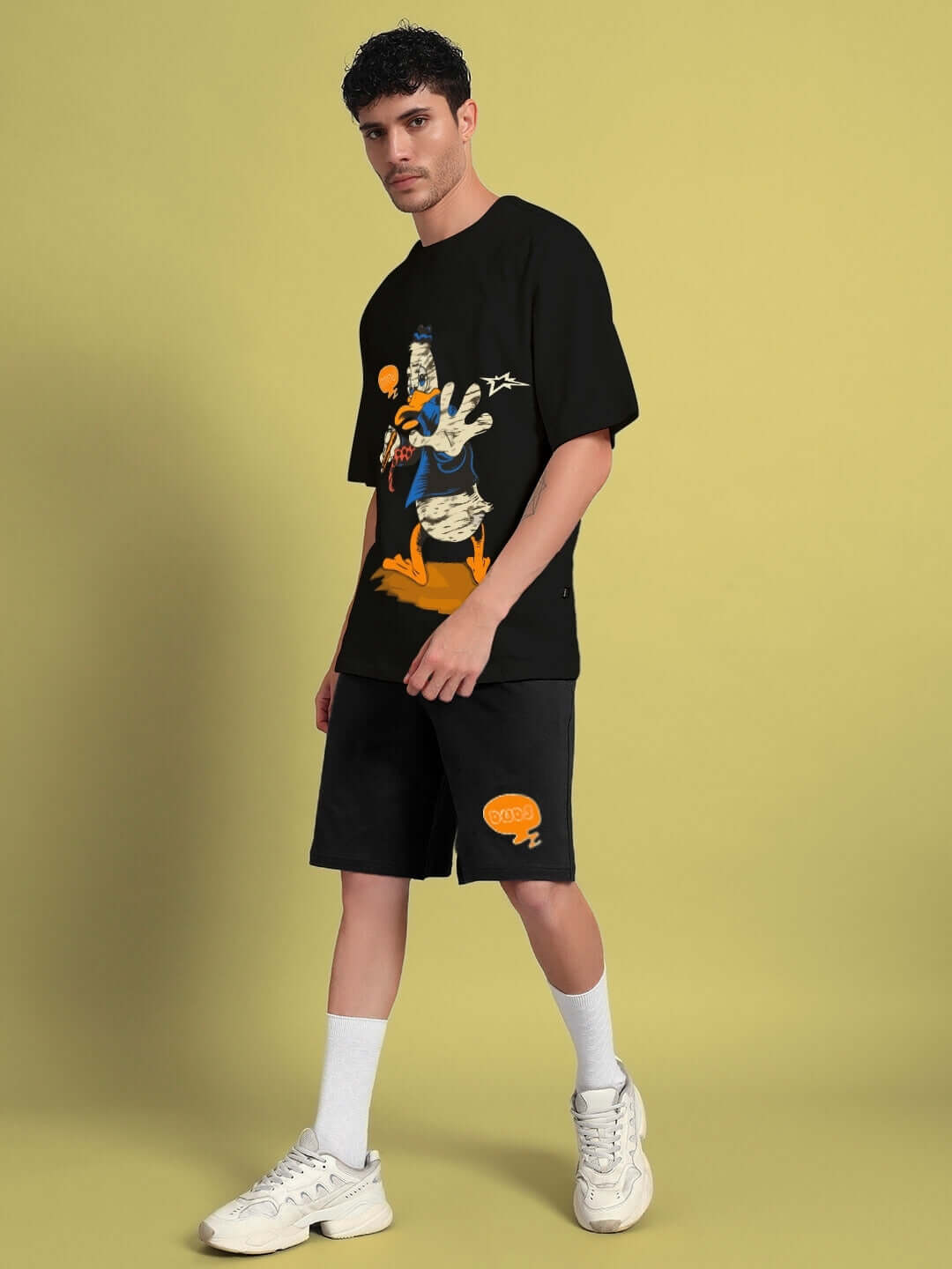 Man wearing the QUACK OFF COTTON CO-ORD SET BLACK, showcasing bold streetwear style with a graphic tee and black shorts.