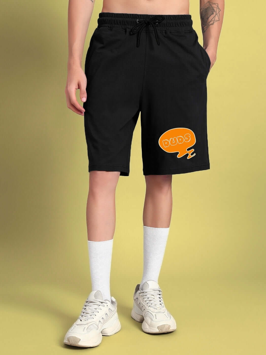 Man wearing black QUACK OFF summer shorts by DUDS, featuring orange logo, customizable for perfect fit. Casual summer fashion.