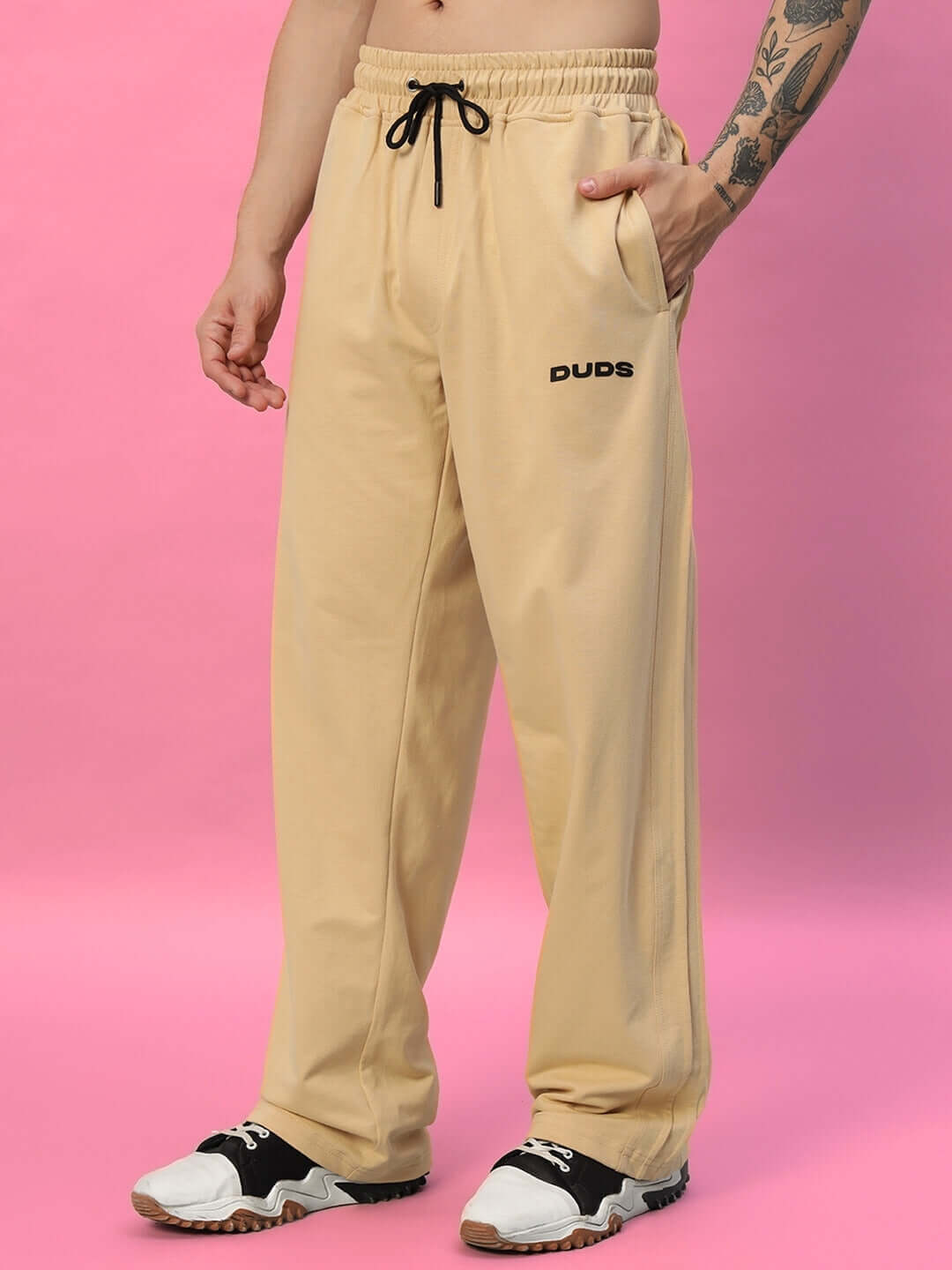 Model wearing Quantum Relaxed-Fit Beige Joggers by DUDS with customizable size options, front view against pink background.