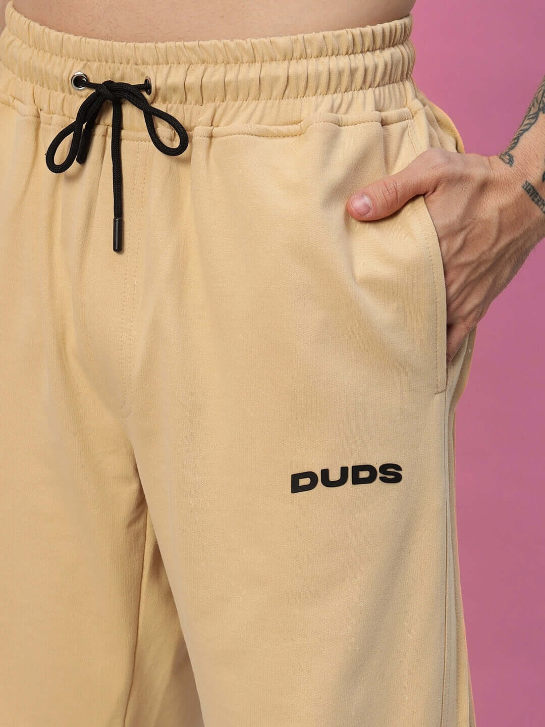 Close-up of Quantum Relaxed-Fit Joggers in beige with black drawstring and DUDS logo, shown in a casual style.