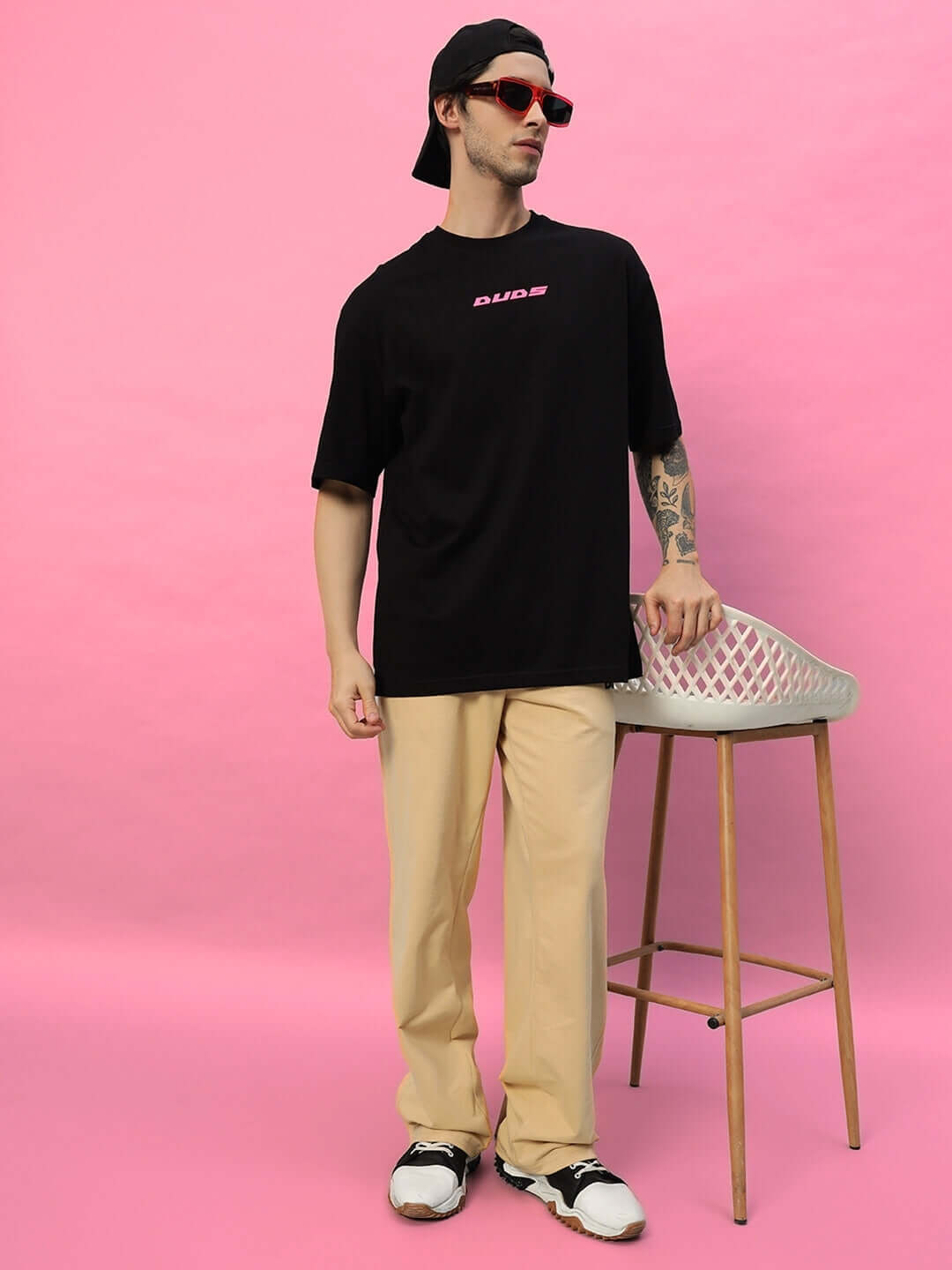 Man wearing Quantum Relaxed-Fit Joggers in beige with black t-shirt and red sunglasses, standing against a pink background.
