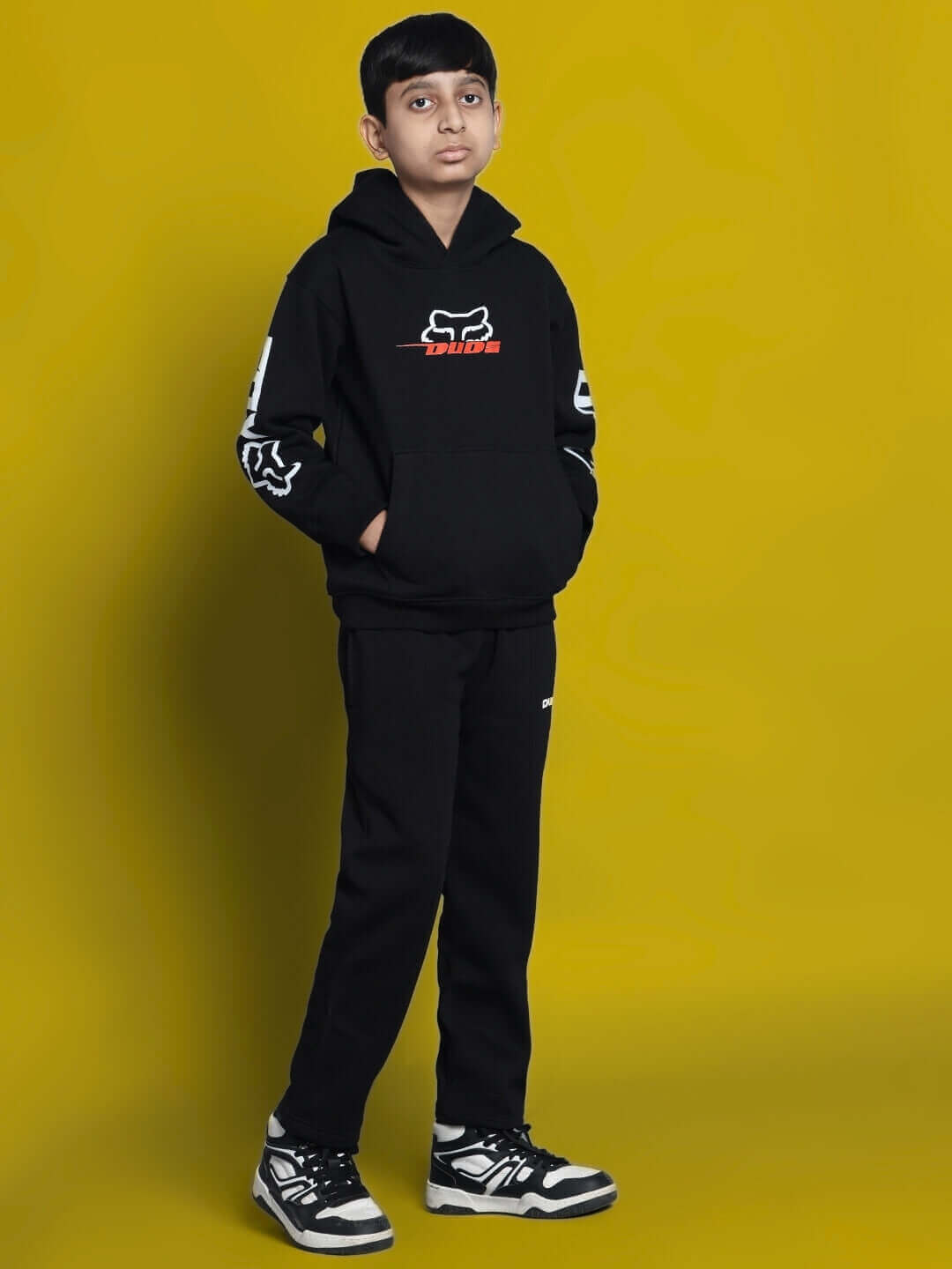 Boy wearing Racing Fox Oversized Hoodie in black with fox graphics, streetwear style for kids, full-length view against yellow background.