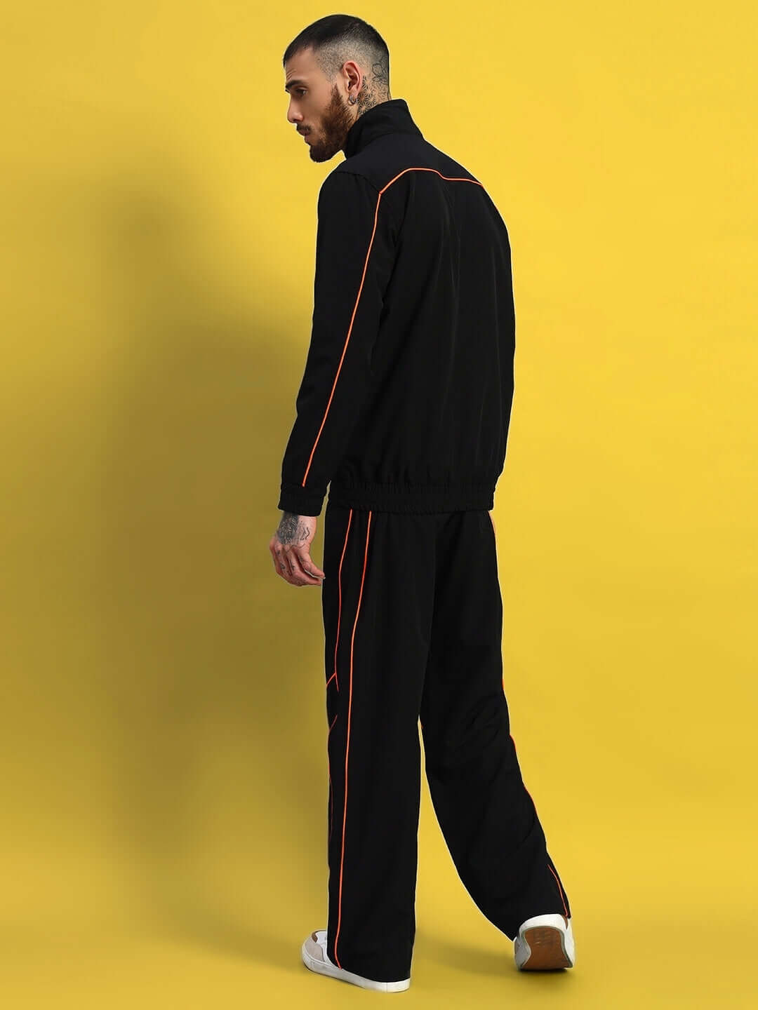 Man wearing black Raider Jacket with red seams, standing against yellow background, showcasing full view of the stylish outerwear.