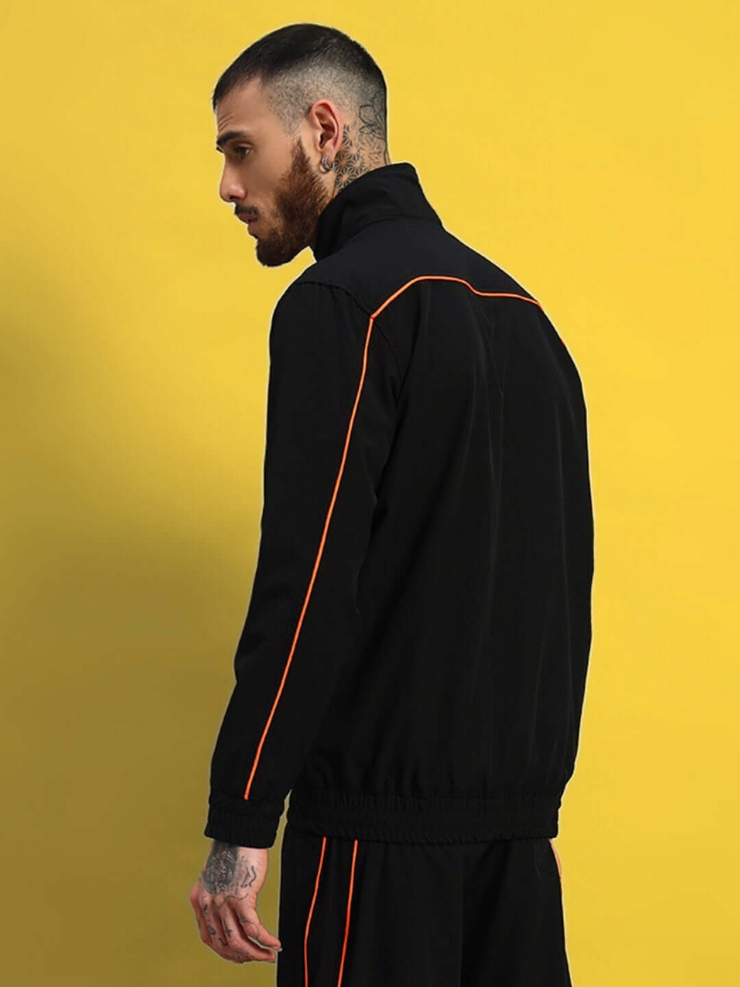 Model wearing black RAIDER jacket with orange piping against a yellow background, showcasing back view and stylish design details.