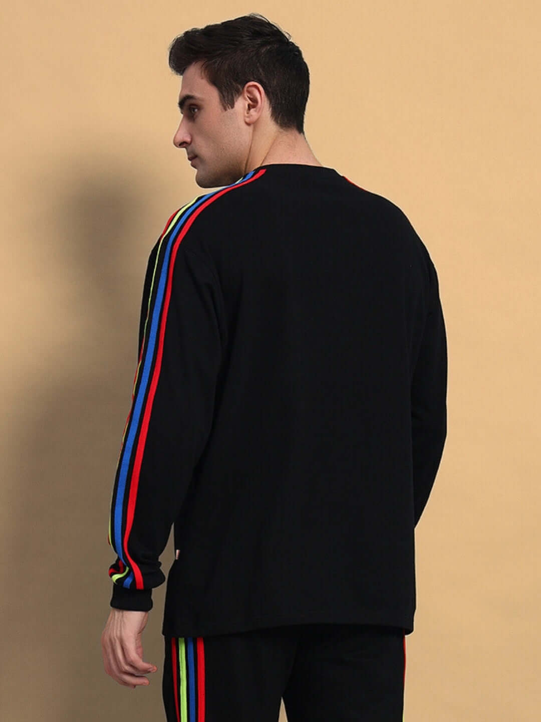 Model wearing black rainbow colorblock sweatshirt by DUDS, featuring vibrant stripes down the sleeves, highlighting back view details.