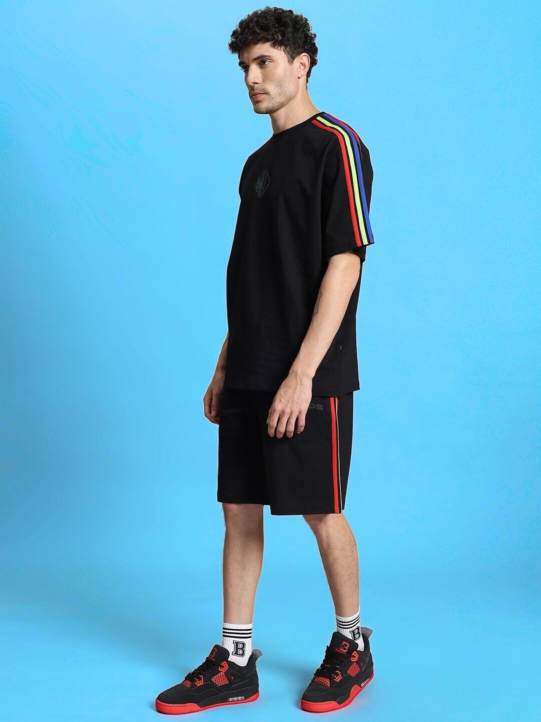 Model wearing RAINBOW SUMMER CO-ORD SET BLACK with rainbow accents, showcasing streetwear style on a blue background.