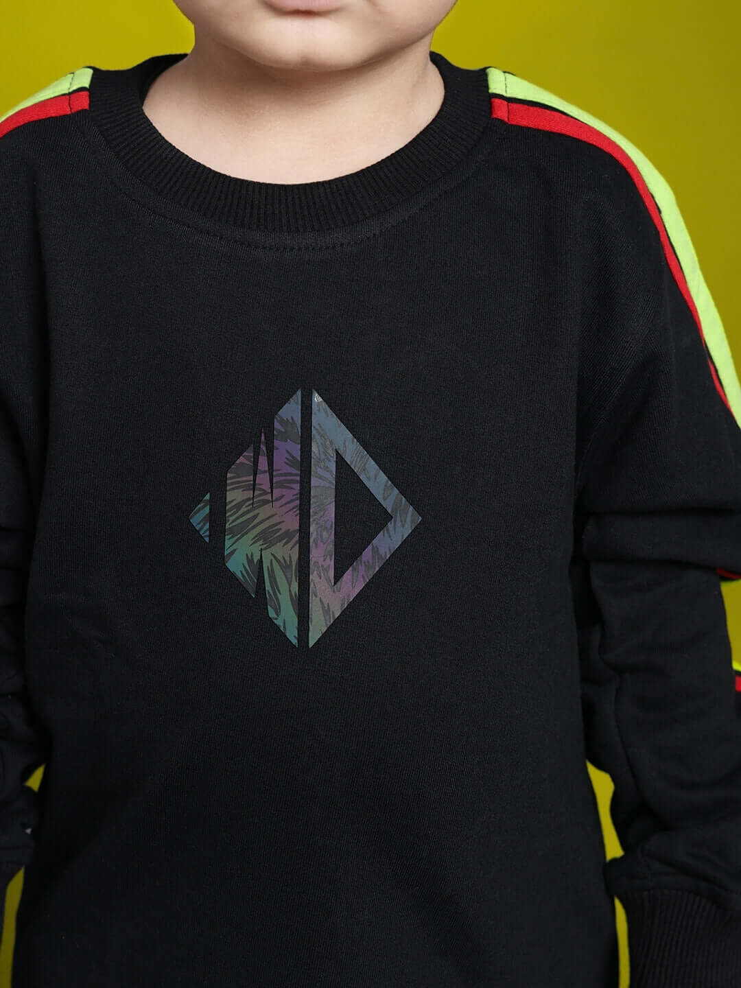 Child wearing a black unisex rainbow co-ord set with colorful striped sleeves and geometric logo on the front.