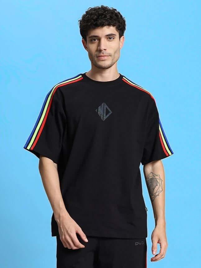 Black rainbow oversized t-shirt with colorful stripes on sleeves, made from premium cotton and elastane. Modeled against a blue background.