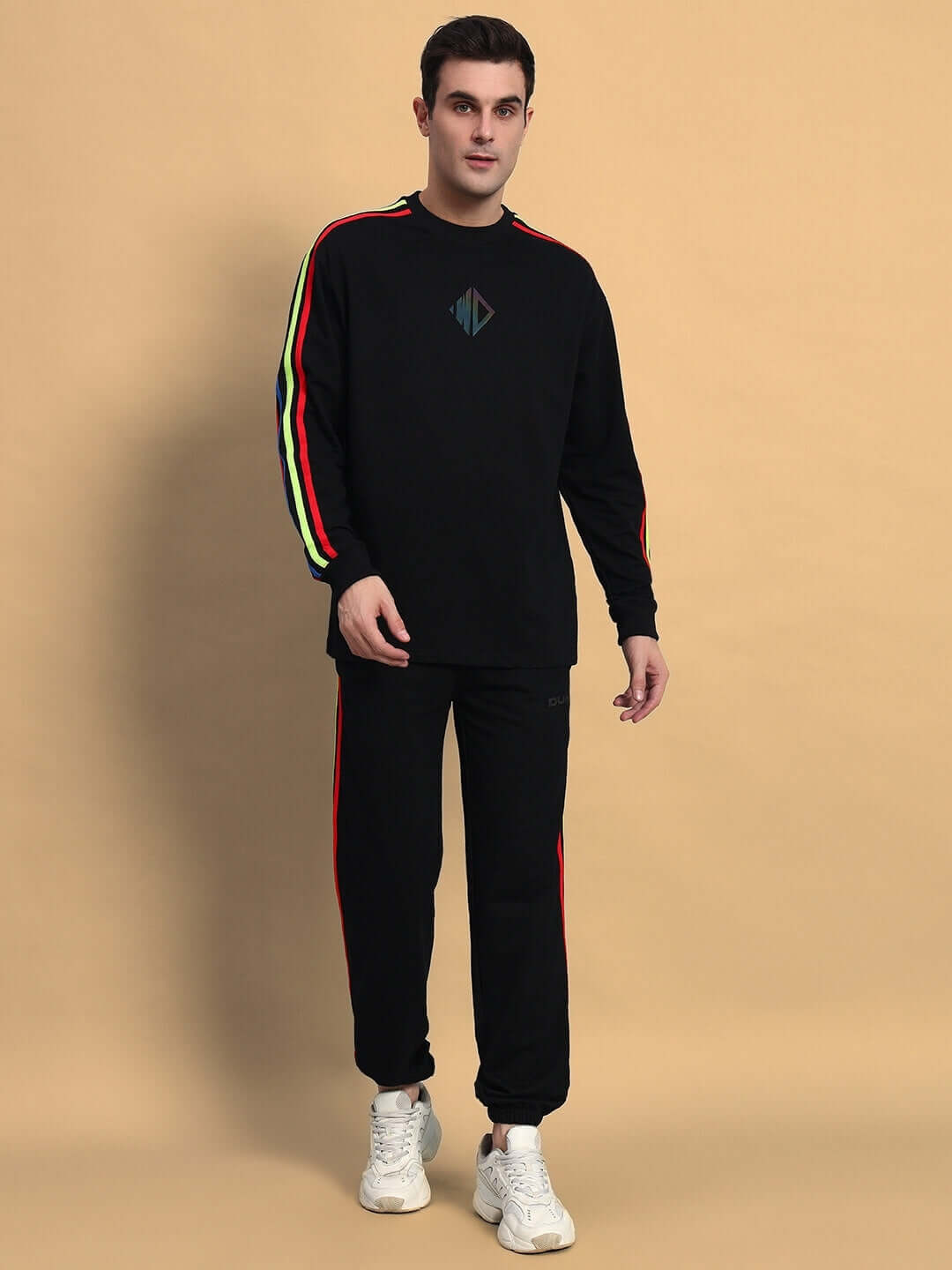 Model wearing RAINBOW OVERSIZED CO-ORD SET BLACK with colorful striped sleeves, relaxed fit joggers, and white sneakers.