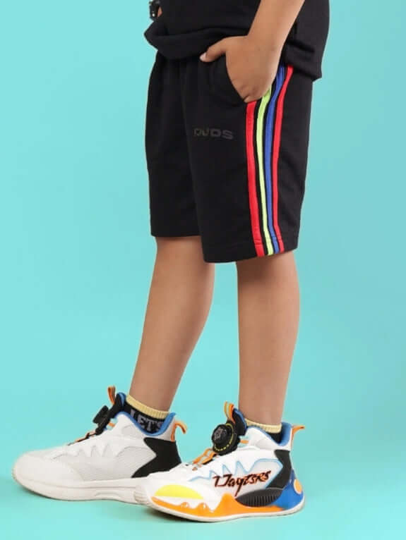 Child wearing RAINBOW SHORTS FOR BOYS & GIRLS BLACK with colorful side stripes and sneakers.