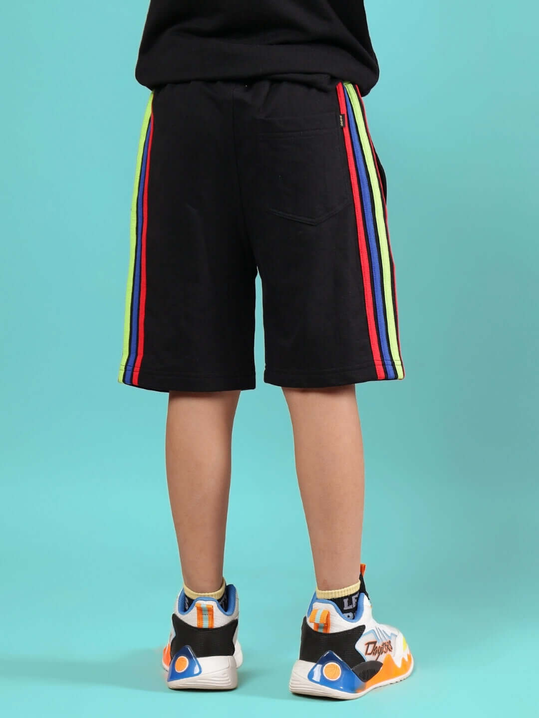 Child wearing RAINBOW SHORTS FOR BOYS & GIRLS BLACK, standing back view with colorful stripes, showcasing custom fit option.
