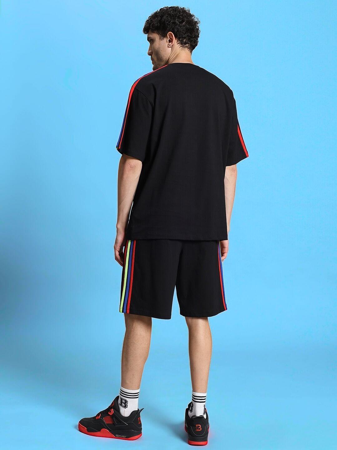 Model wearing RAINBOW SUMMER CO-ORD SET BLACK with rainbow accents, showcasing streetwear style on blue background.