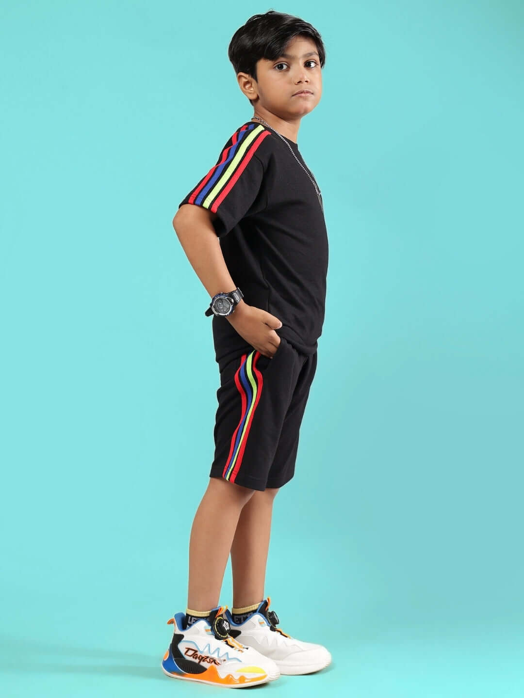 Child wearing RAINBOW SUMMER CO-ORD FOR BOYS & GIRLS BLACK with stripes and sneakers, against a blue background.