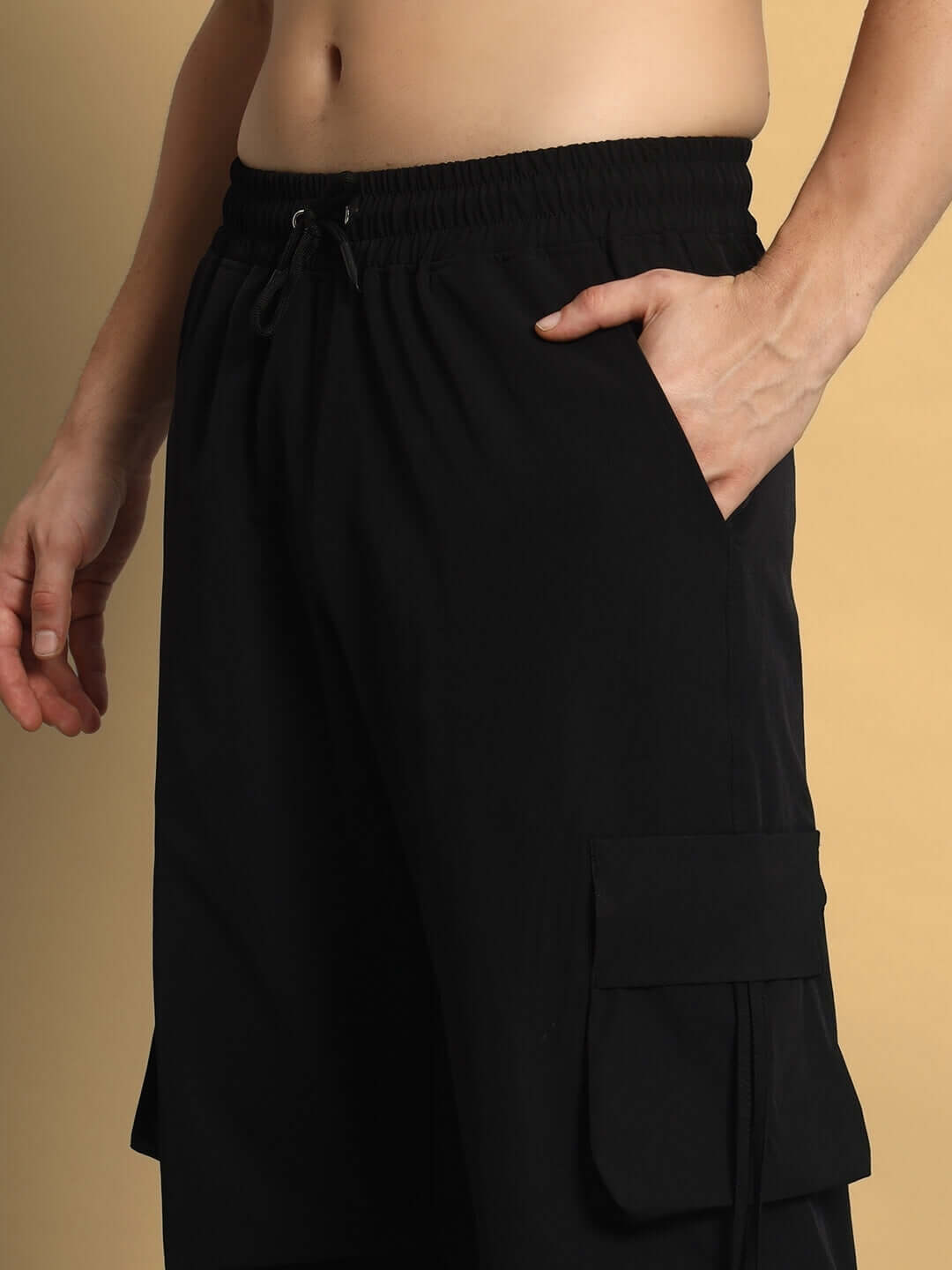 Close-up of model wearing RAMROD black parachute cargo pants with pockets, showcasing elastic waistband and relaxed fit.