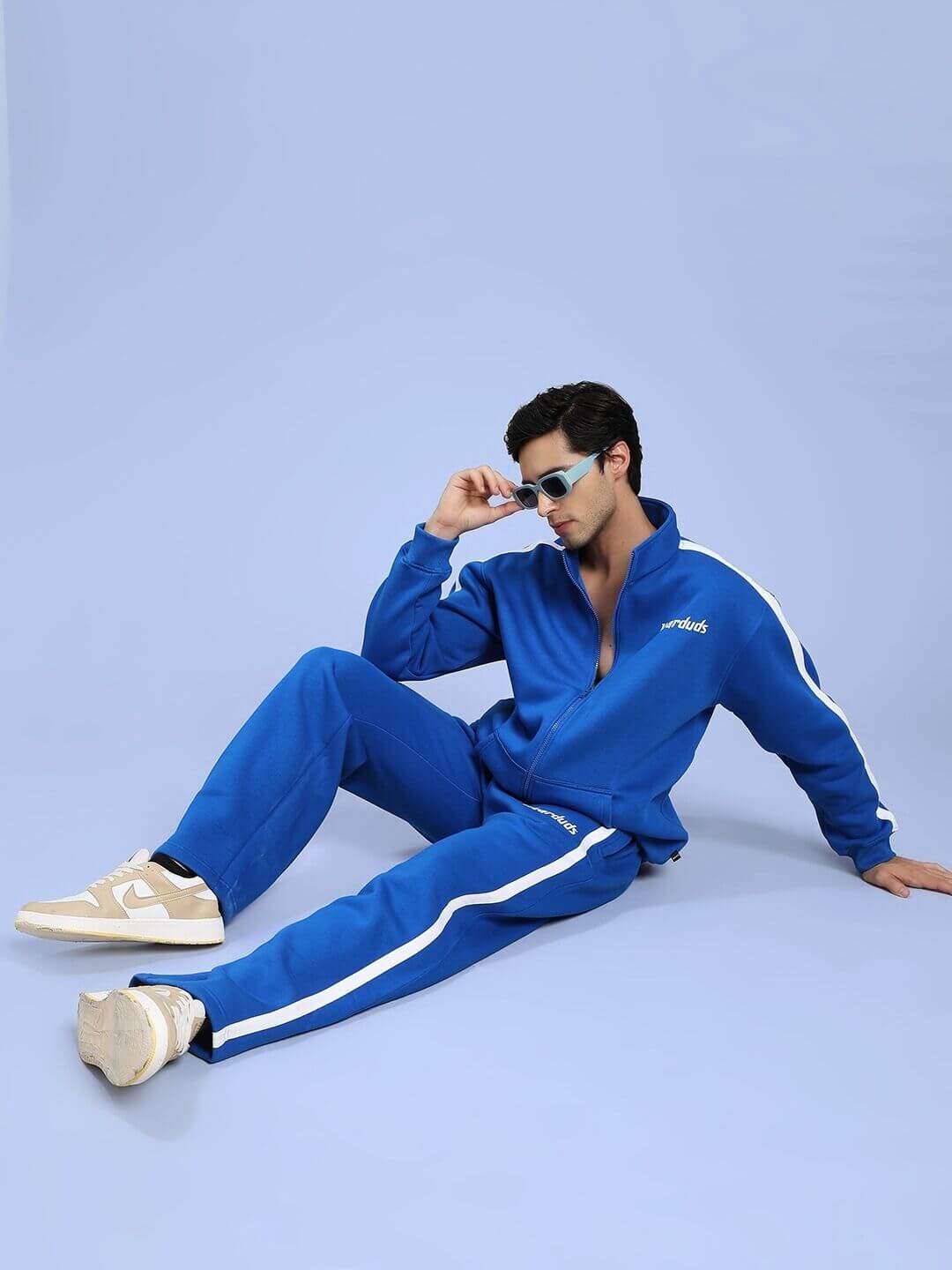 Model wearing RAPID STRIDE ROYAL BLUE COTTON FLEECE CO-ORD SET sitting against blue background.