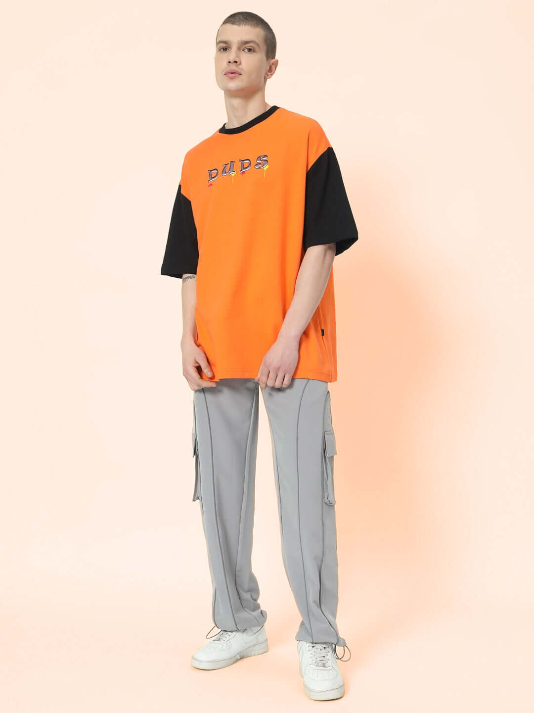 Model wearing RAY REFLECTOR parachute cargo pants in grey, paired with an orange and black DUDS top, featuring side pockets and a relaxed fit.
