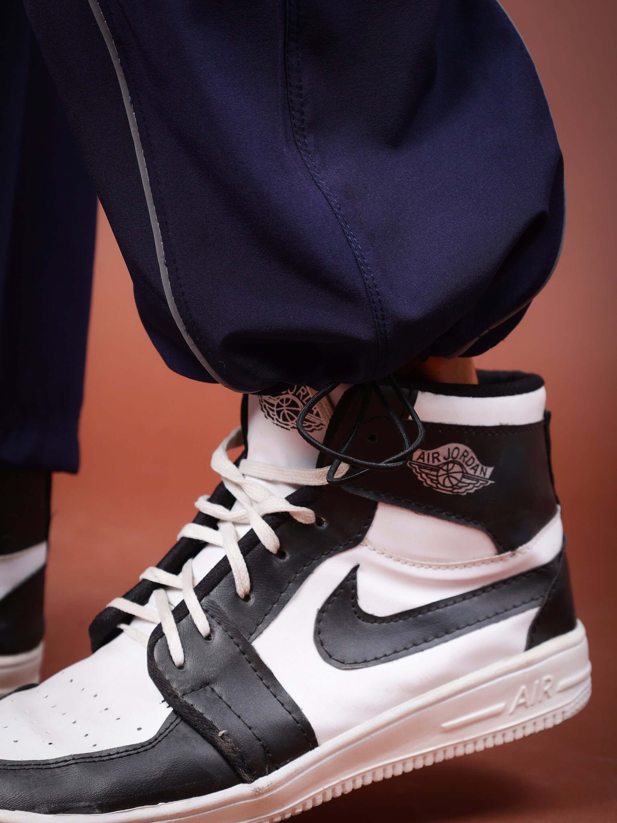 Close-up of navy blue Ray Reflector Parachute Cargo Pants paired with black and white sneakers, highlighting reflective stripe detail.