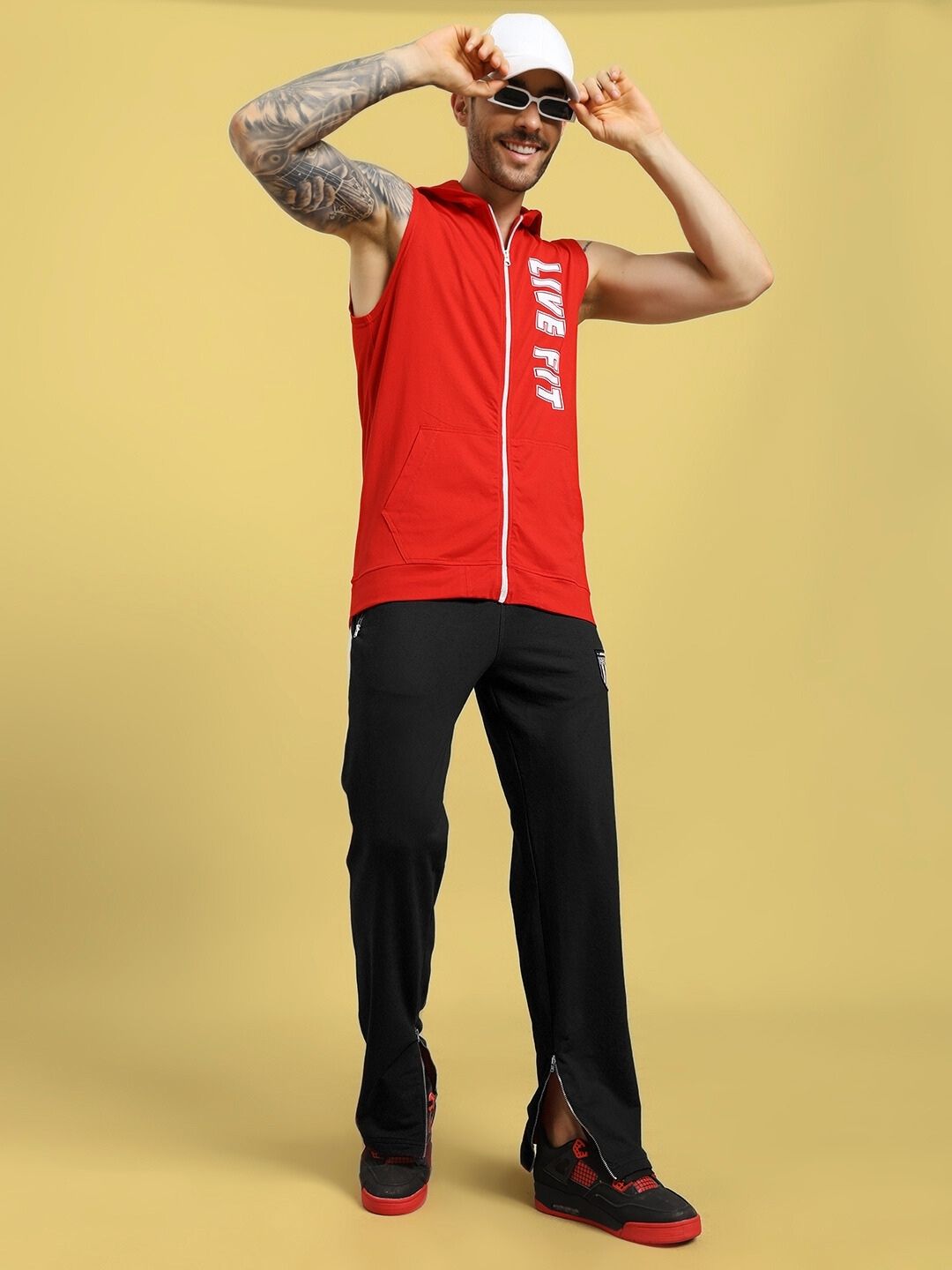 Man modeling red sleeveless hoodie and black pants with "LIVE FIT" text, posing against yellow background, casual fitness wear style.