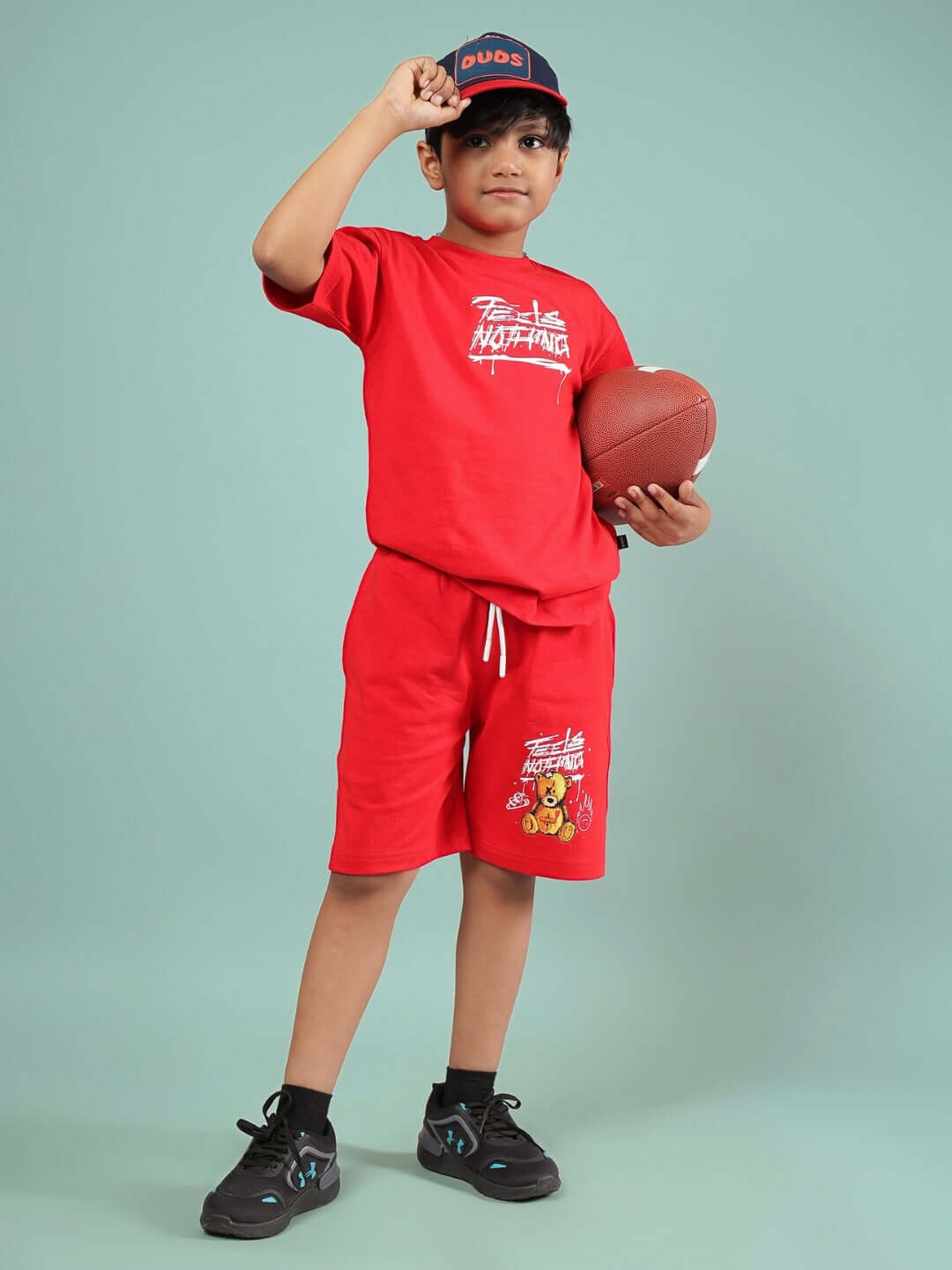 Child wearing red FEELS NOTHING co-ord set holding a football, showcasing customized fit by DUDS Tailors suitable for boys and girls.