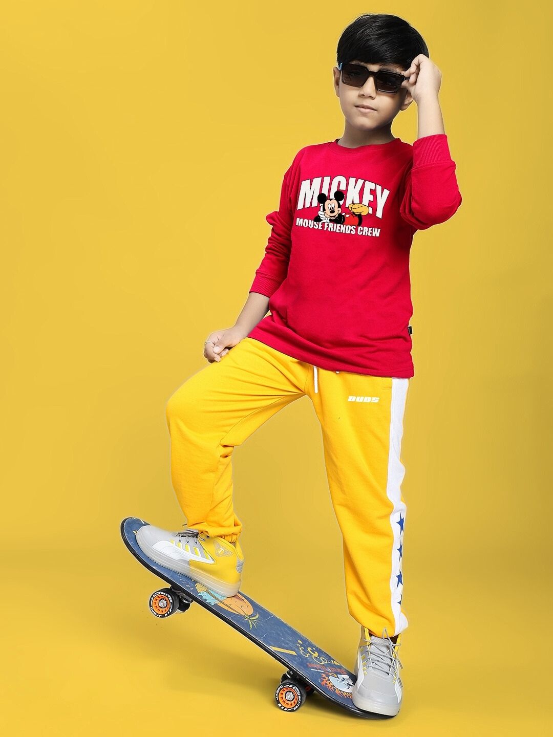 Child wearing Friends Crew Print Sweatshirt for Boys Girls Red, posing with skateboard against yellow background.