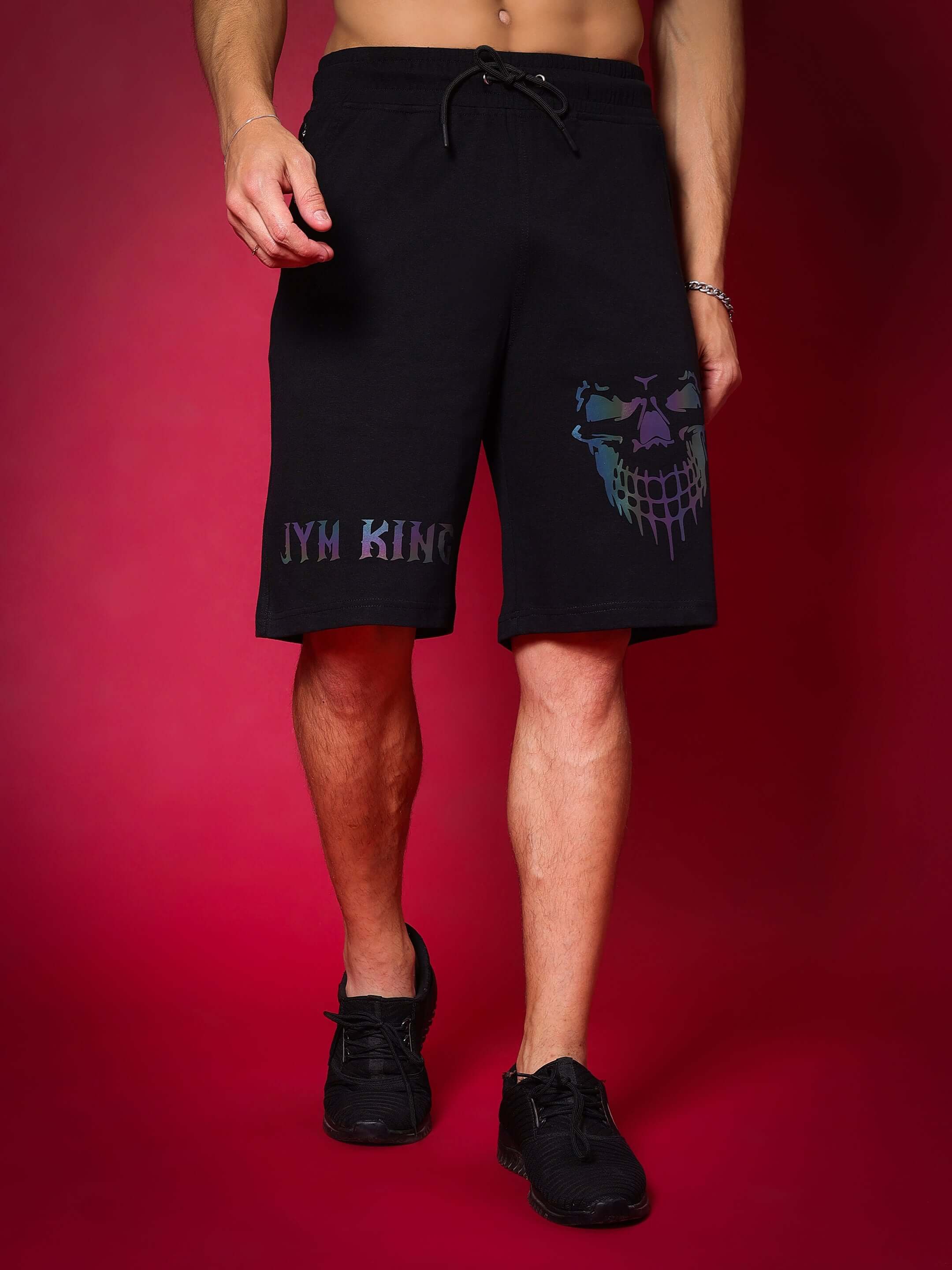 Man wearing black REFLECTOR JYM KING shorts, showcasing regular fit and custom fit options against a red background.