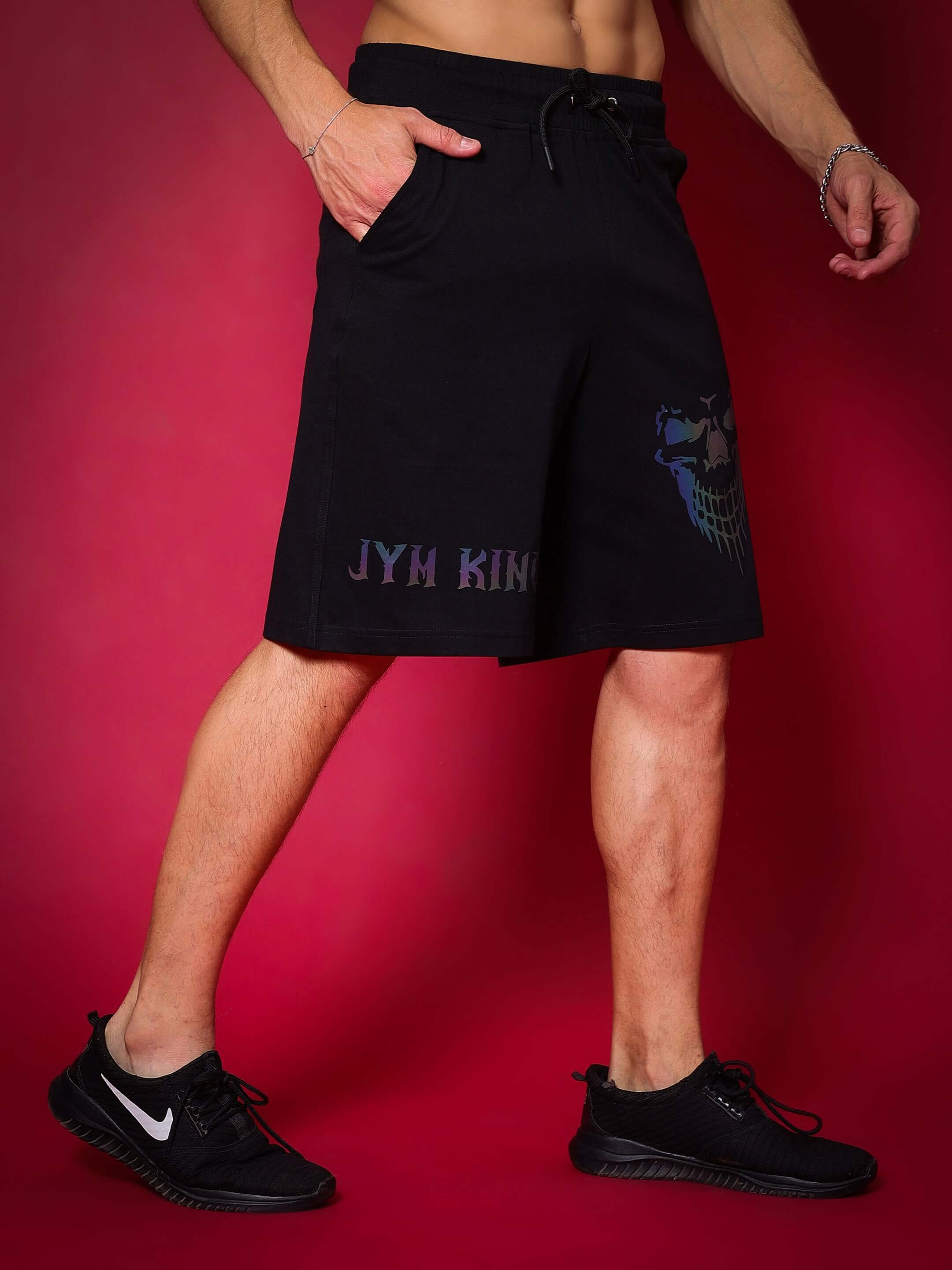 Model wearing black JYM KING Regular Fit Shorts, showcasing custom fit option against red background, styled with black sneakers.