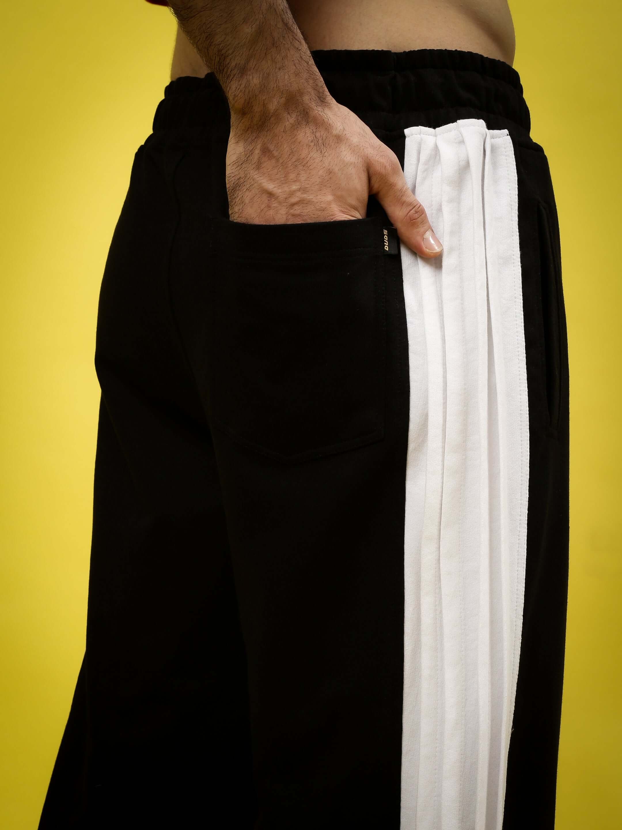Close-up of black and white REGAL BAGGY JOGGERS featuring custom fit options by DUDS, highlighted against a vibrant yellow background.