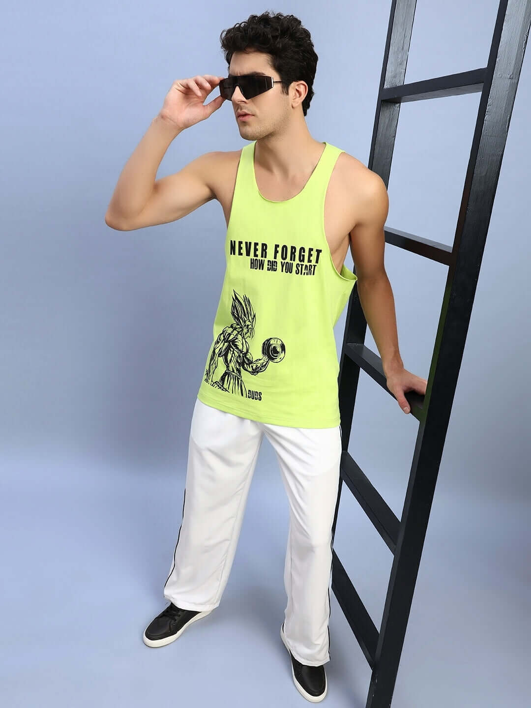 Man in a neon green tank top and white relaxed-fit joggers posing with black sunglasses