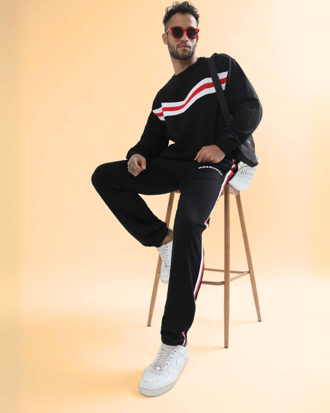 Unisex model wearing RIGHTMAN oversized co-ord set with red & white contrast panels, sitting on a stool. Comfortable, stylish, and premium cotton.