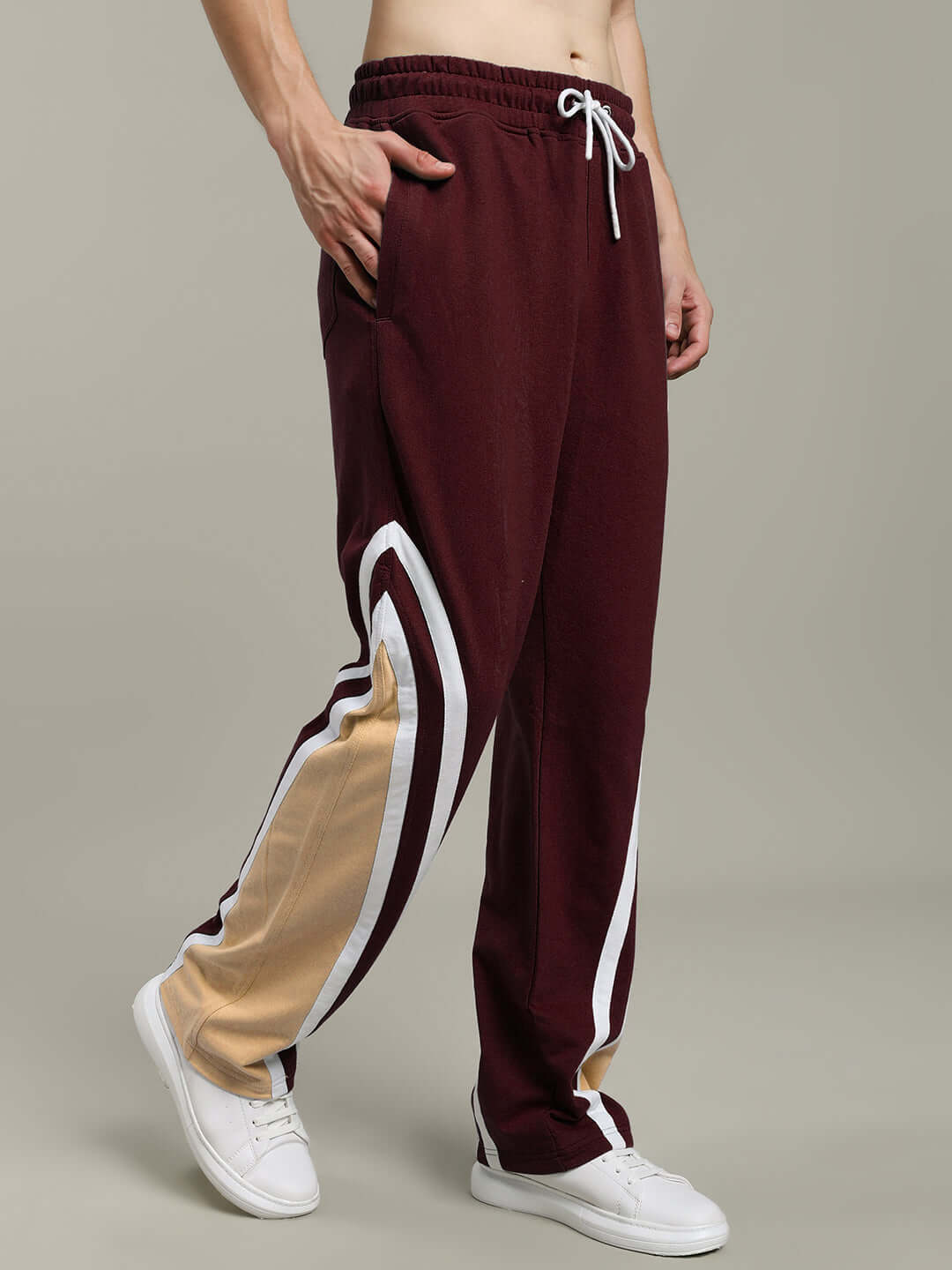 Men's relaxed fit joggers in brown with white and beige side stripes, featuring a drawstring waist and paired with white sneakers.