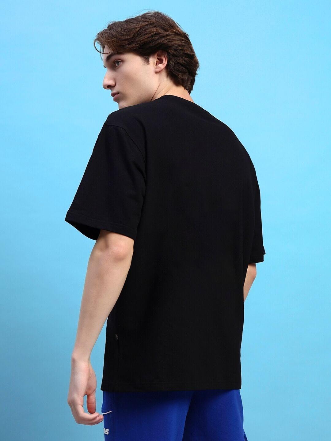 Rear view of model wearing Roaring Thunder Printed Oversized Black T-shirt made from premium cotton fabric, against blue background.