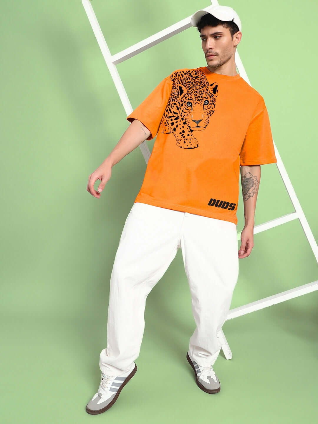 Model wearing bold ROBERTO LEOPARD PRINTED T-SHIRT ORANGE with leopard graphic and casual white pants for a standout streetwear look.