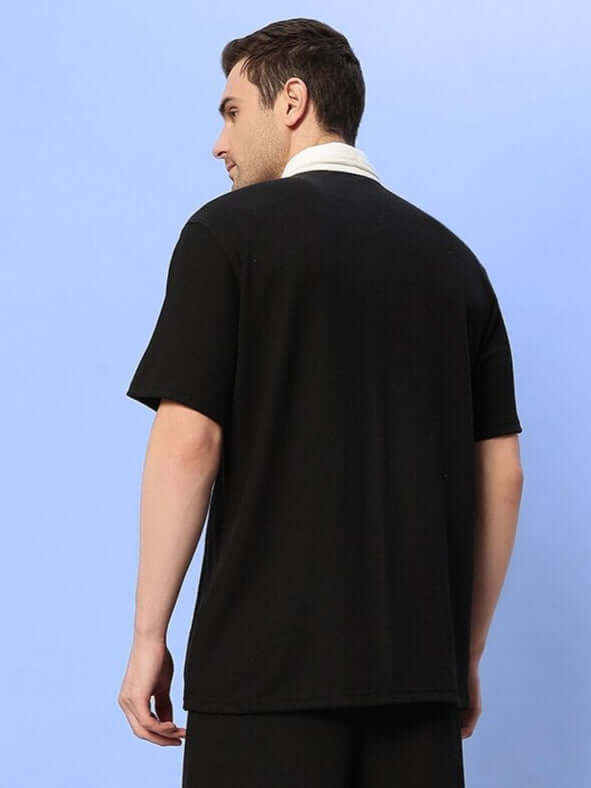 Rear view of a man wearing a black Robson regular fit shirt made of waffle fabric, showcasing short sleeves, set against a light blue background.