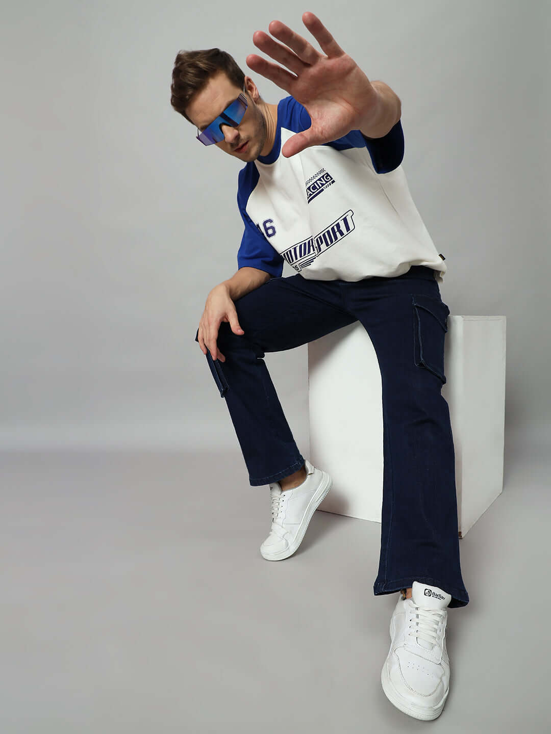 Person wearing navy denim cargo jeans and white sneakers, posing with hand raised against a gray background.