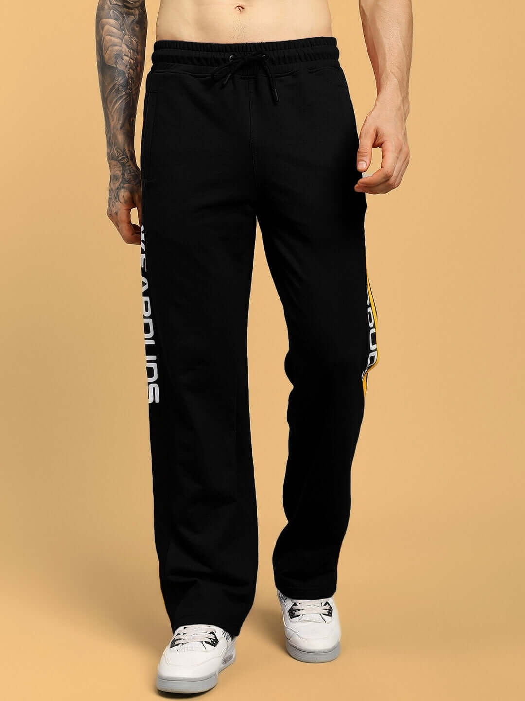 Man wearing black joggers with lettering, displaying relaxed-fit style and comfortable design, ideal for custom fitting by DUDS Tailors.