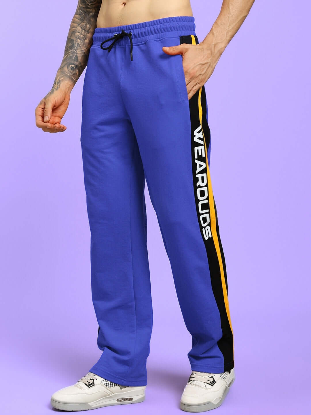 Model wearing blue ROGER relaxed-fit joggers with yellow stripe and WEAROUS logo, showcasing comfortable fit and trendy design.