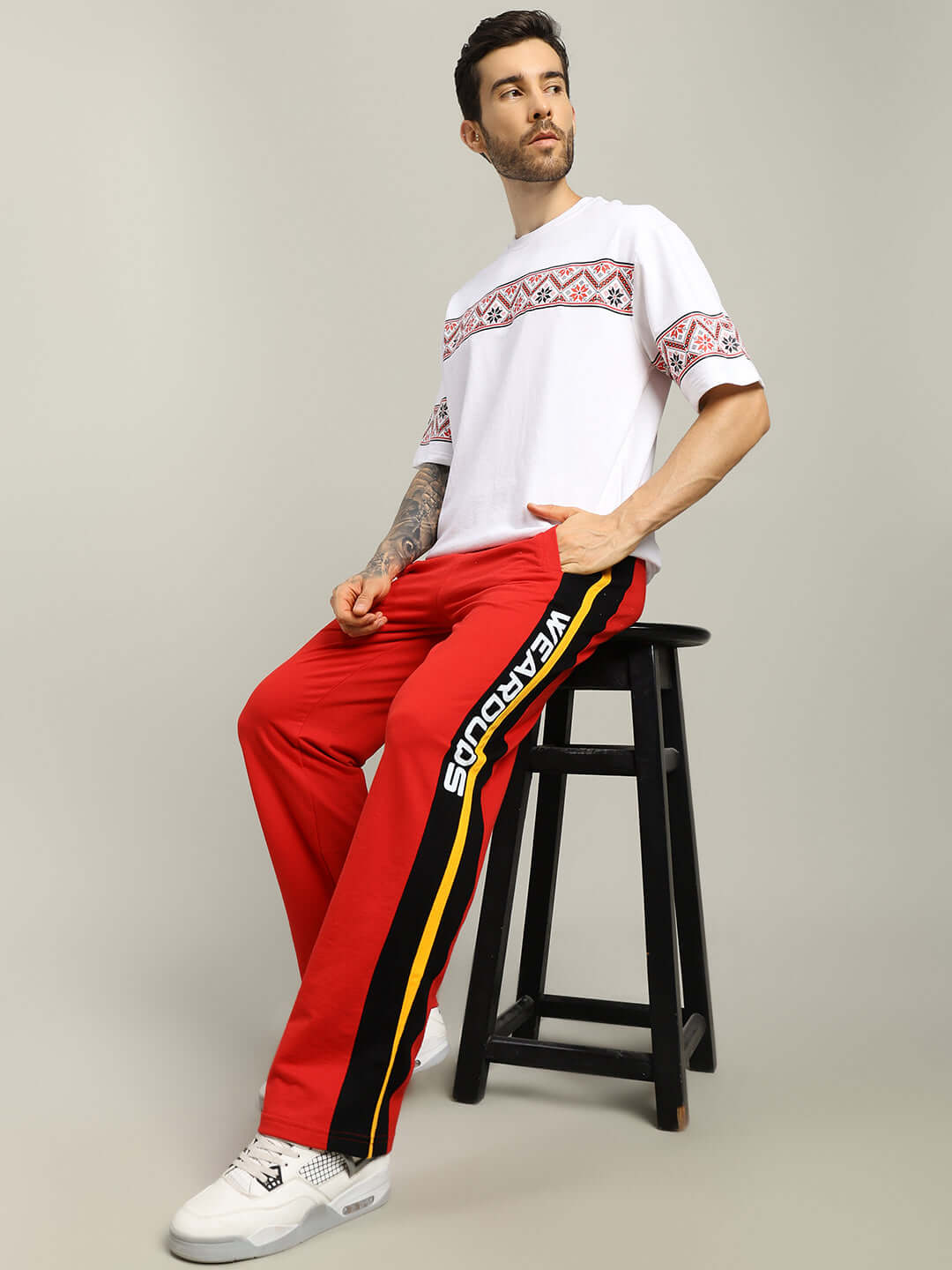 Man wearing ROGER RELAXED-FIT JOGGERS RED MEN seated on stool in stylish casual outfit.