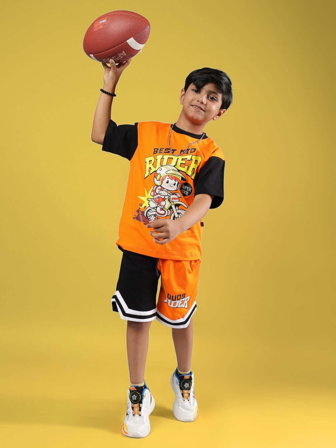 Boy wearing orange and black Rogue Rider co-ord set while holding a football, showcasing stylish kids' fashion by DUDS.