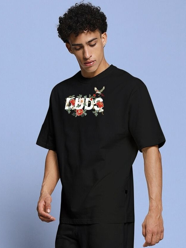 Young man wearing ROSE CHARM OVER-SIZED T-SHIRT BLACK with floral graphic design.