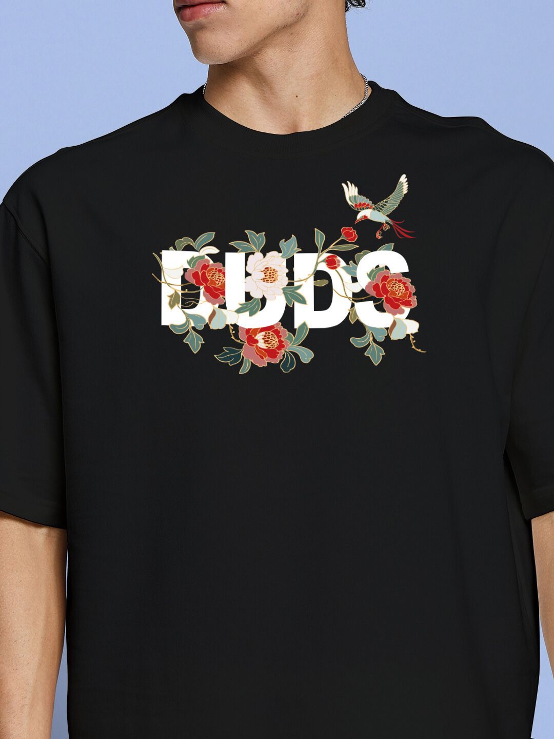 Man wearing ROSE CHARM OVER-SIZED T-SHIRT BLACK with floral graphic print on chest.