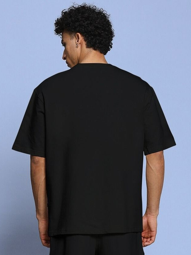 Back view of ROSE CHARM OVER-SIZED T-SHIRT BLACK worn by a model, showcasing its fit and design.