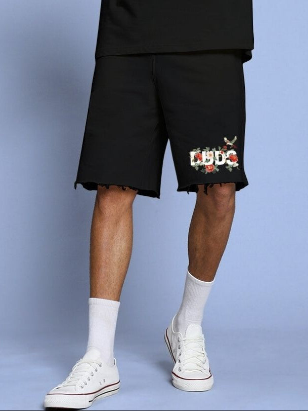 Model wearing ROSE CHARM RELAXED FIT SHORTS BLACK with floral design on a light blue background.