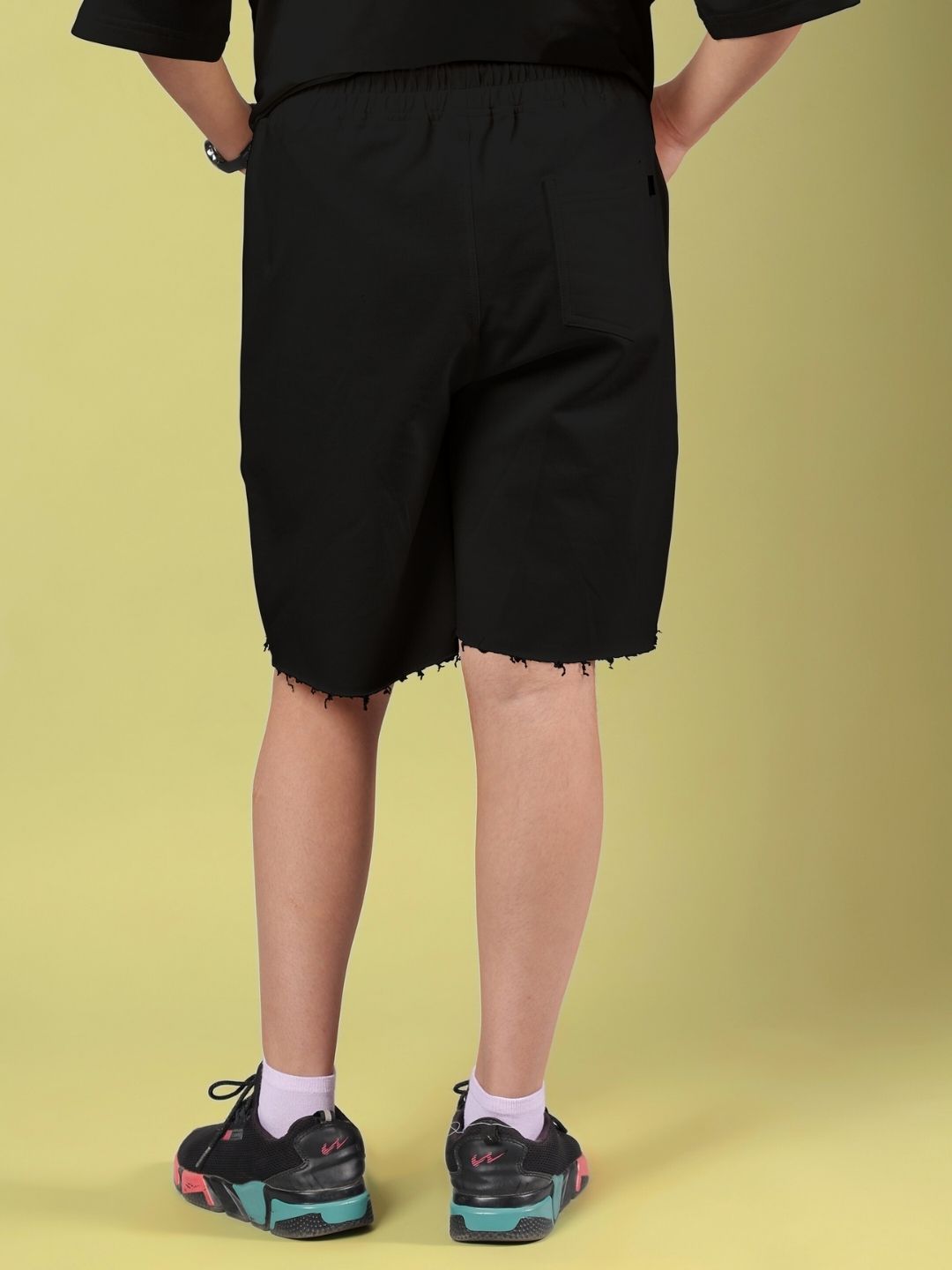 Back view of ROSE CHARM SHORTS FOR BOYS AND GIRLS BLACK worn with sneakers and socks, showcasing casual style.