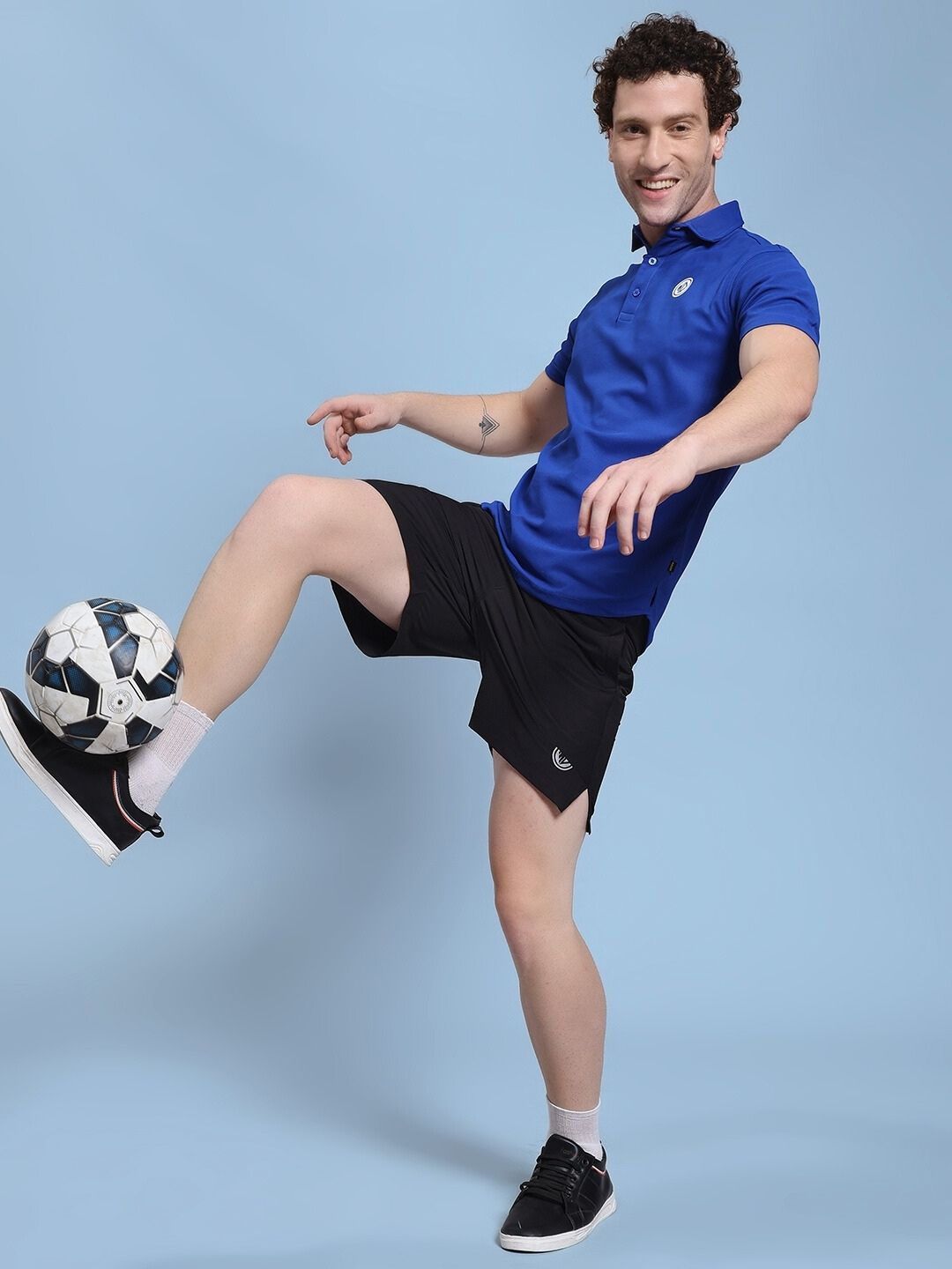 Person wearing ROSEWOOD POLO REGULAR FIT T-SHIRT BLUE playing soccer indoors.