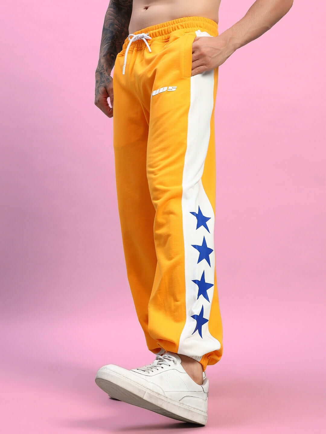 Model wearing ROX PRIMER Relaxed Fit Joggers in orange and white with blue stars, highlighting comfort and style for active wear.