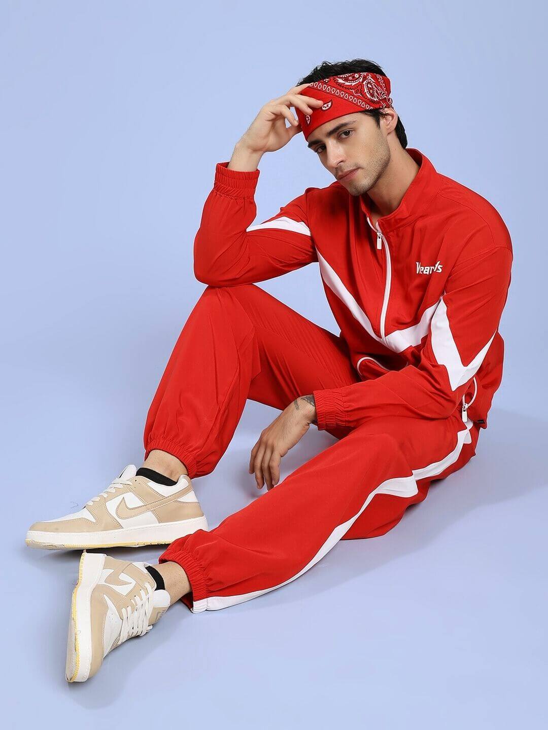Man wearing ROYAL COMFORT RELAXED FIT JOGGER RED sitting on floor, styled with red bandana and jacket, showcasing loungewear style.
