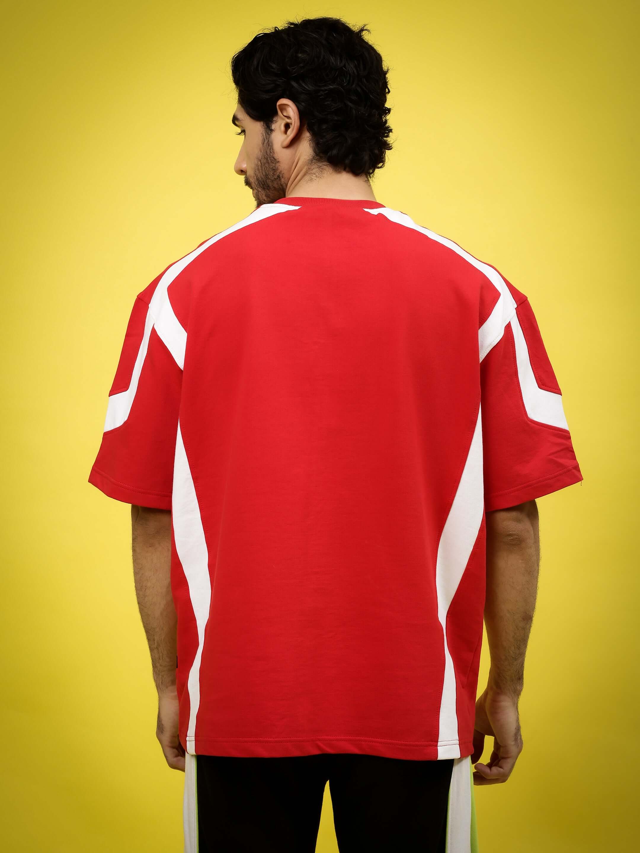 Back view of Rugby Over-Sized T-Shirt in red with white stripes, made from premium cotton blend fabric. Model stands against yellow background.